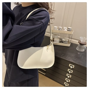 Close-up of white minimalist hobo bag with gold zipper held by model in navy sweater