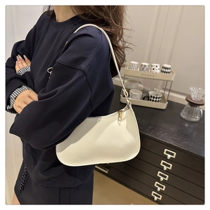 Detail of minimalist cream baguette bag with gold zipper shown on a model's shoulder