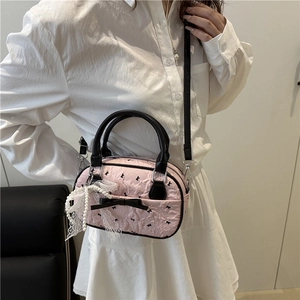 Pink textured crossbody bag with black bows and pearl lace pendant on a female model