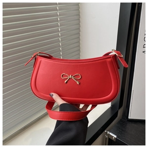 Detail of red PU leather baguette bag featuring a gold metal bow and adjustable strap