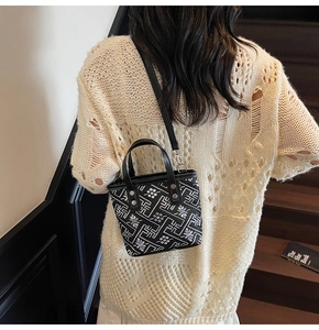 Detail of black mini bucket bag with geometric patterns worn with a cream sweater