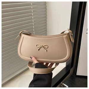 Detailed shot of beige baguette bag featuring a gold bow hardware and matte leather