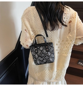 Detail of black leather bucket bag with white floral patterns and sturdy handles