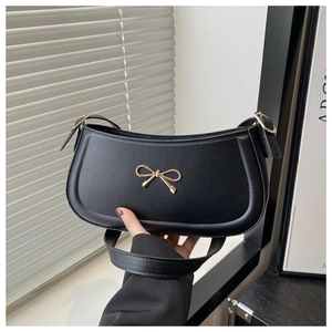 Detail of a black half-moon shoulder bag with a gold metal bow charm and leather texture