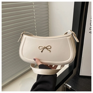 Close-up of golden metal bow buckle on a beige cream leather underarm bag detail