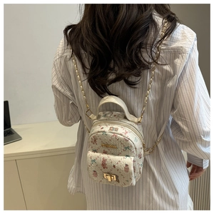 Detail of mini floral backpack with bear prints and gold chain strap on blue striped shirt