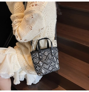 Detail of embroidered geometric patterns on black canvas bucket bag with shoulder strap