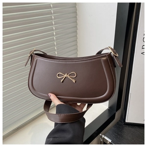 Close-up of the elegant gold bow metal buckle on a dark coffee faux leather shoulder bag