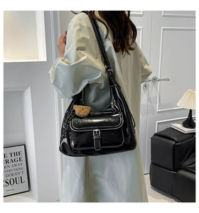 Close-up of black glossy leather tote bag with buckle detail and a brown bear charm