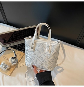 Detail of white bucket bag with traditional embroidery on desk with laptop and headset