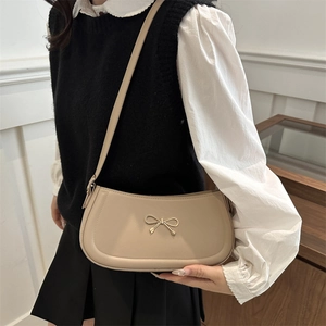 Beige baguette underarm bag with gold bow decoration shown on model shoulder