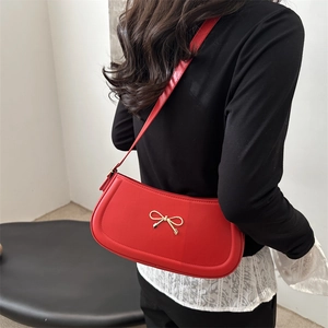 Red half-moon underarm bag with gold bow decoration and leather texture on a model