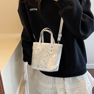 White geometric patterned bucket bag with adjustable strap worn by model in casual style