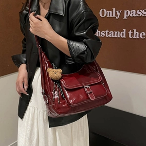 Minimalist burgundy patent leather tote bag with plush bear charm worn by a model
