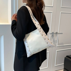 Sac fourre-tout en cuir blanc avec œillets dorés porté par un mannequin en costume