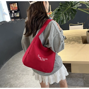 Detail of red canvas tote bag with white C'est la vie text worn on the shoulder