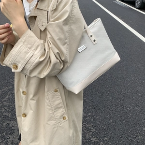 White woven tote bag with leather trim and shoulder straps shown on a model