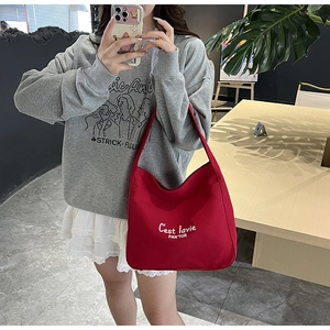 Close-up of a large wine red tote bag with white typography carried by a model