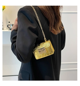 Detail of gold faux-crocodile mini chain bag with metallic lock worn on a black blazer