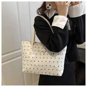 Detail of cream tote bag with embossed texture and black bow print with gold charm