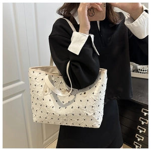 Detail view of white tote bag with black bow embroidery and golden buckle accent