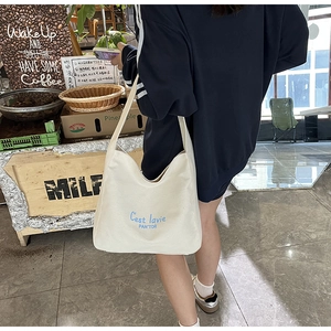White large canvas tote bag with blue C'est la vie text worn on a woman's shoulder