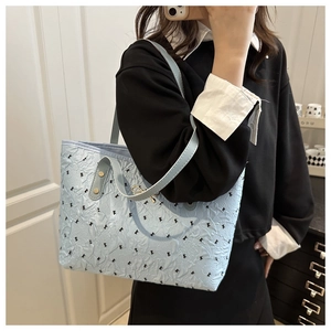 Close-up of light blue pleated tote bag with black bow embroidery and gold hardware detail