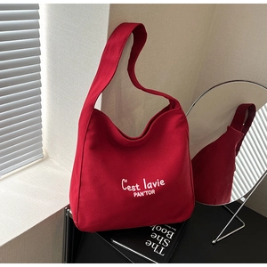 Detail of red canvas tote bag with white lettering against a minimalist indoor setting