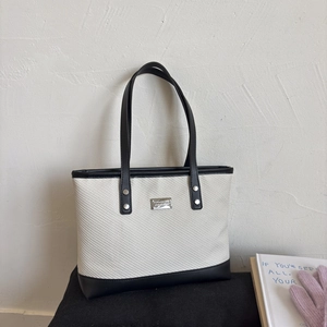 Detail of color-block tote bag featuring cream woven fabric and black leather trim