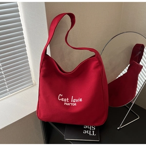 Detail of red canvas tote bag with C'est lavie embroidery in a stylish indoor setting