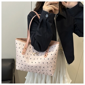 Detailed view of pink tote bag with black bow patterns and gold metallic charm on model