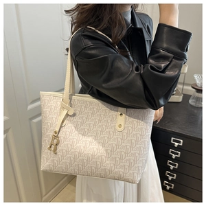 Détail du sac cabas beige avec imprimé lettres et pendentif R doré attaché à la poignée