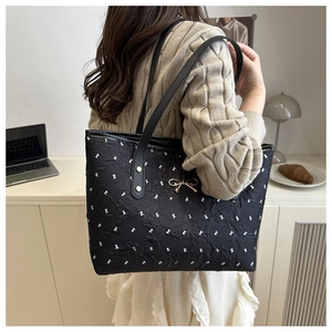 Detail of black quilted tote bag with white bow prints and gold metal bow charm