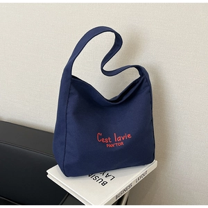 Detail of navy blue canvas bucket bag featuring red C'est lavie artistic lettering