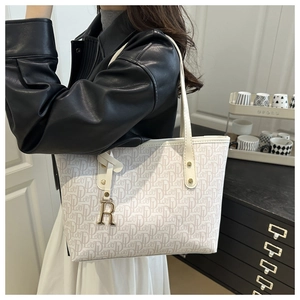 Détail d'un grand sac cabas crème avec motif monogramme et pendentif lettre R doré