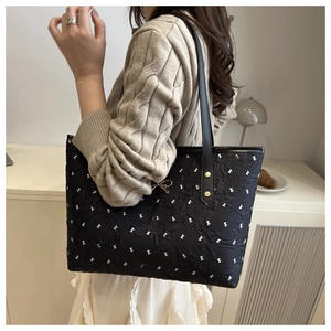Detail of black pleated tote bag with white bow patterns and gold bow charm detail