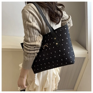 Detail of black tote bag with white bow prints and gold butterfly pendant worn by model