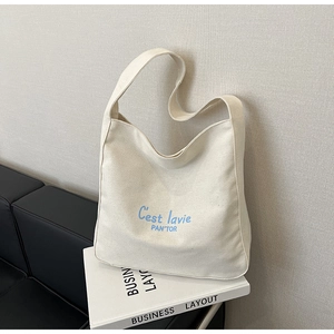 Close-up of cream canvas tote bag with blue C'est la vie text on a stylish sofa