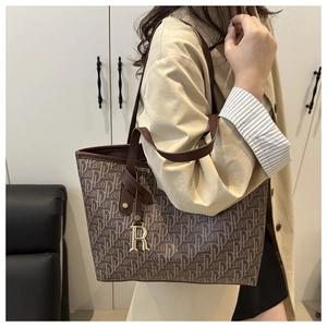 Gros plan du sac cabas monogramme avec bordure en cuir et pendentif R doré porté à l'épaule