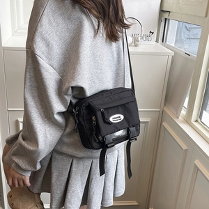 Fashionable black nylon crossbody bag with buckle detail shown in a casual lifestyle setting