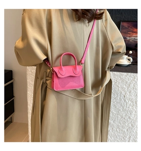 Détail d'un mini sac bandoulière rose fuchsia texturé porté avec un trench-coat kaki