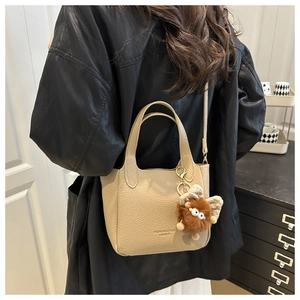 Détail du sac seau beige en cuir avec breloque peluche et longue bandoulière réglable