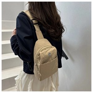 Close-up of khaki nylon chest bag with adjustable wide strap on a model against white stairs