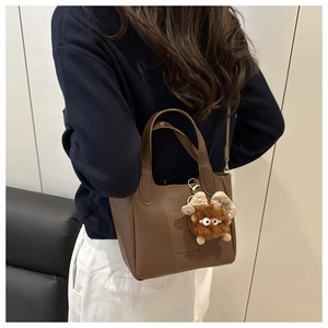 Détail du sac seau en cuir caramel avec texture grainée et charm petit monstre