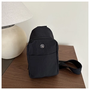Detail of black nylon chest bag with zippers and metal logo on a wooden surface