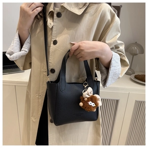 Détail d'un sac seau en cuir noir grainé avec un pendentif en peluche et une bandoulière
