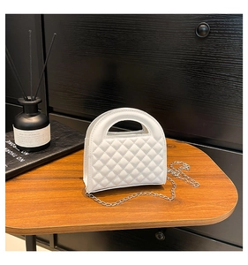 Macro view of white quilted faux leather handbag with silver chain strap on table