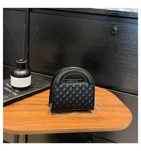 Macro detail of black quilted faux leather crossbody bag with silver chain strap