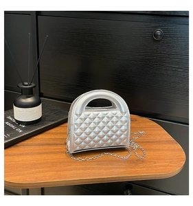 Close-up of silver mini chain bag with quilted pattern and metal strap on wooden surface