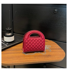 Detail of red quilted mini bag with silver chain strap on a wooden surface